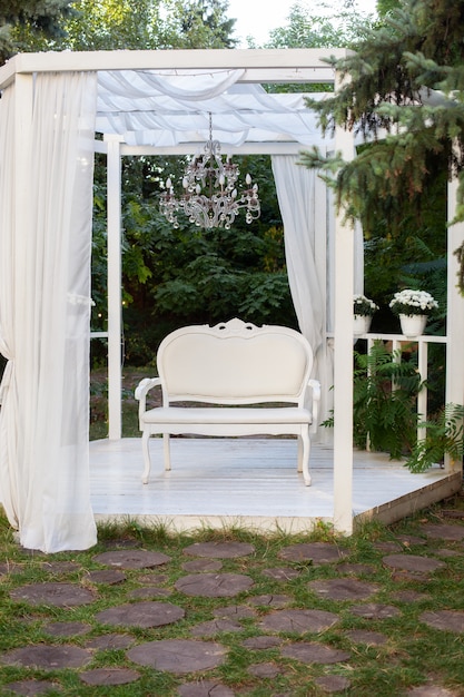 Sommerpavillon mit weißen vorhängen. nische gibt es terrasse, auf der ein weißes sofa im stil der provence oder rustikal.