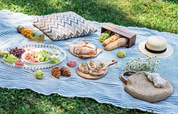 Sommerpicknick auf dem Rasen, Sandwiches mit Lachs, Trauben, Backwaren und Früchten