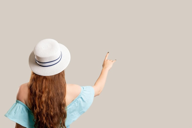 Sommerreise Urlaubsreise Frau in schulterfreiem blauem Kleid und weißem Hut, die auf den Kopierbereich zeigt, der auf neutraler Rückseite isoliert ist Urlaubsoutfit Werbehintergrund