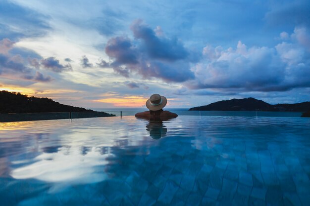 Sommerreiseferienkonzept, glückliche reisende asiatische Frau mit Hut und Bikini entspannen im luxuriösen Infinity-Poolhotel