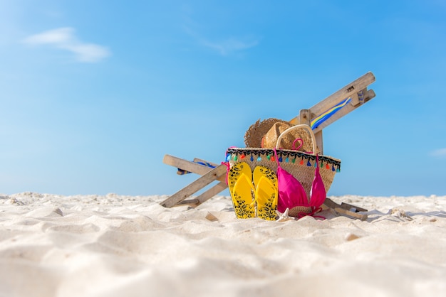 Sommerreisen. Bikini und Flipflops, Hut, Fischstern und Tasche nahe Strandstuhl auf sandigem Strand gegen blauen See- und Himmelhintergrund, Kopienraum. Sommerferien-Konzept