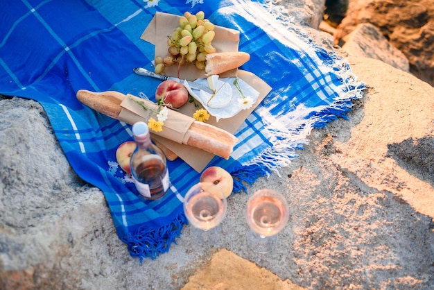 Sommerromantisches Picknick mit Obst, Käse, Wein, Brot, Trauben, Pfirsich. Licht von den ersten Sonnenstrahlen.