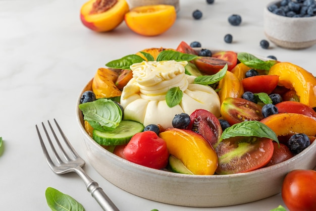 Sommersalat mit Burrata-Käse, gegrillten Pfirsichen, Tomaten, Blaubeeren, Gurken, Olivenöl und Basilikum