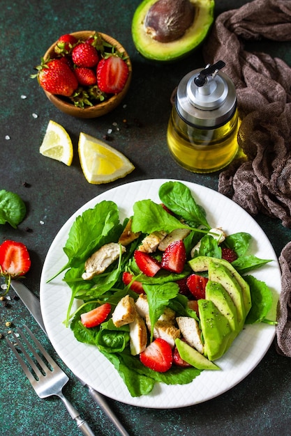 Sommersalat mit Erdbeeren, gegrilltem Hähnchen und Avocado auf einem Steintisch Draufsicht flach gelegt