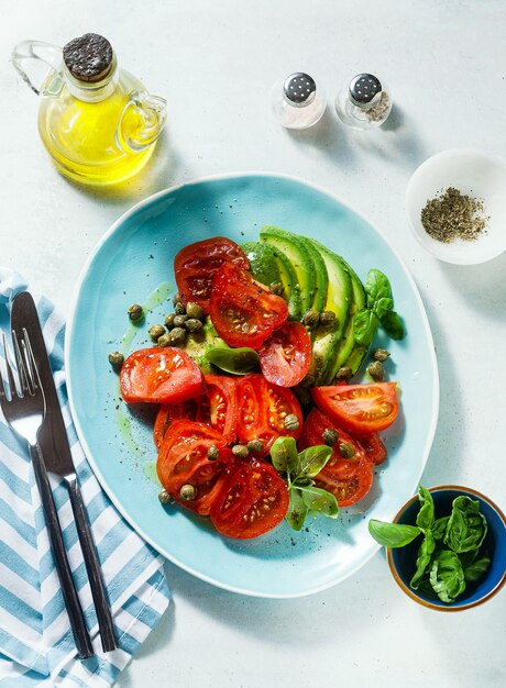 Sommersalat mit reifen Tomaten und Avocado mit Kapern in einem blauen Teller auf dem Tisch