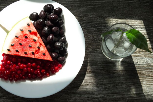 Sommersnack Frische Beeren und Früchte auf einem Holztisch mit grünen Pflanzenblättern