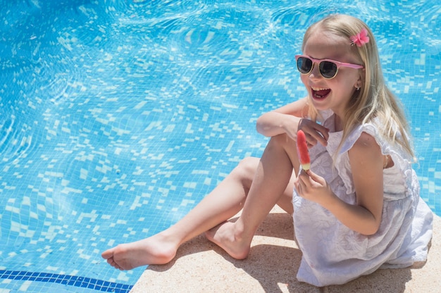 Sommerspaß. Glückliches kleines Mädchen, das Eis nahe dem Pool isst