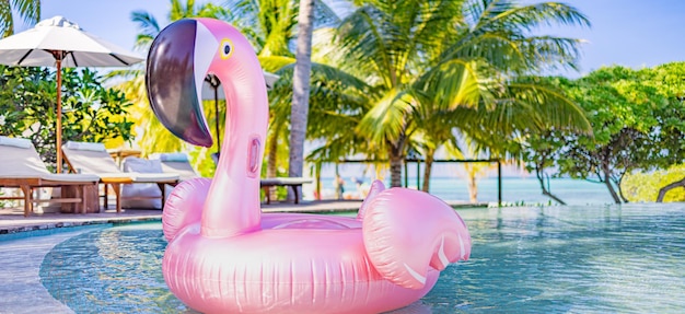 Sommerspaß im tropischen Resort, Stühle, Liegestühle, Sonnenschirm unter Palmen. Rosa aufblasbarer Flamingo