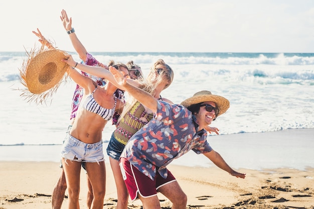 Sommerstilgruppe junger fröhlicher Leute, die zusammen Spaß haben und viel lachen im Urlaubsurlaub am Strand - Meereswellen und blauer Himmel im Hintergrund - Lebensstil der Touristen