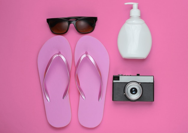 Sommerstillleben. Strandzubehör. Modische rosa Flipflops am Strand, Retro-Kamera, Sonnencremeflasche, Sonnenbrille auf rosa Papier