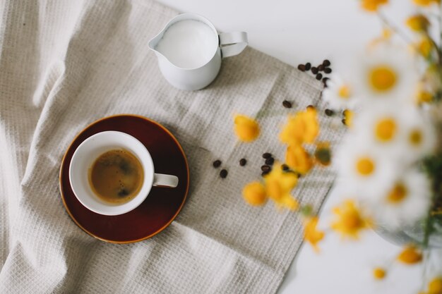 Sommerstillleben-Szene mit Wildblumen, Tasse Kaffee und Milchkrug auf weißem Tisch