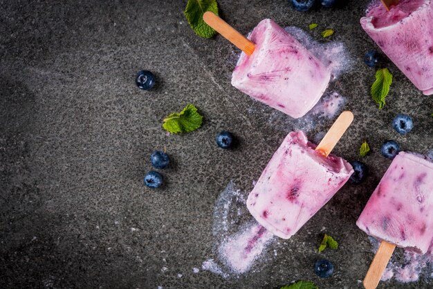 Sommersüßigkeiten und Desserts. Veganes Essen. Gefrorene Getränke, Smoothies. Eis am Stiel aus hausgemachtem griechischem Joghurt und frischen Bio-Heidelbeeren. Mit Minze. Auf schwarzem Steintisch. Ansicht von oben