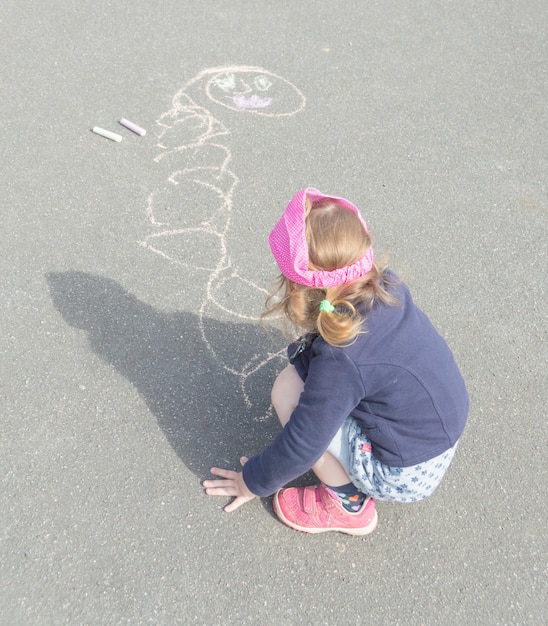 Sommertag auf Asphalt mit Kreide zeichnet ein kleines Mädchen.