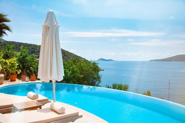 Sommerurlaub am Pool. Veranda mit Liegestühlen und Sonnenschirm mit Meerblick