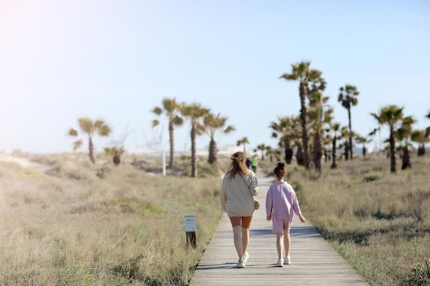 Foto sommerurlaub am strand am meer mutter mit kind mädchen gehen an einem sonnigen tag auf einem holzsteg zwischen palmen hochqualitatives foto