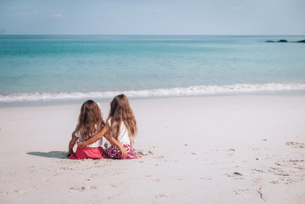 Sommerurlaub. Kleine Mädchen sitzen am Sandstrand und schauen auf das blaue Meer und den Himmel. Reise-, Urlaubs- und Abenteuerkonzept