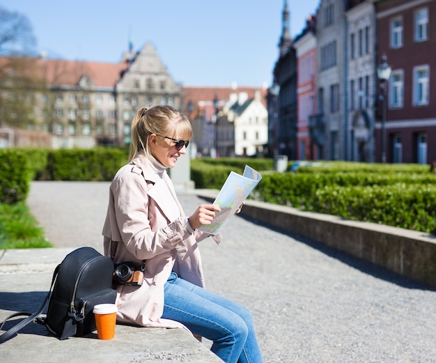 Sommerurlaub und Reisekonzept - glückliche Frau mit Sonnenbrille mit Karte, Rucksack und Kamera in der Altstadt von Tallinn, Estland