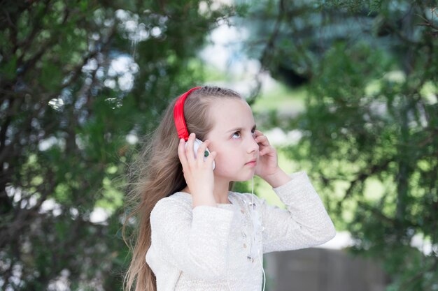 Sommerurlaub und Spaß. Kleines Mädchen hört Musik im Sommerpark. Kinder genießen Musik in Kopfhörern im Freien. Modekind und moderne Technologie. Melodie-Sound und mp3.