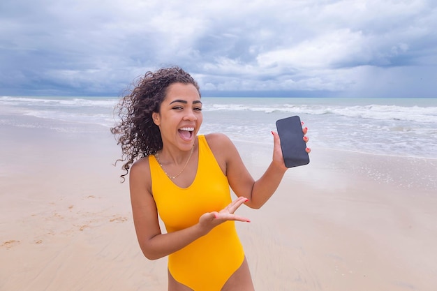 Sommerurlaubstechnologie und Internetkonzept Afro-Frau mit Handy mit leerem Bildschirm am Strand