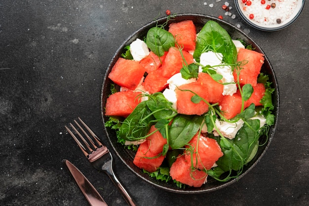 Sommerwassermelonen-Salatschüssel mit Ziegenkäsespinat und Erbsensprossen auf Draufsicht-Kopienraum des grauen Tabellenhintergrundes