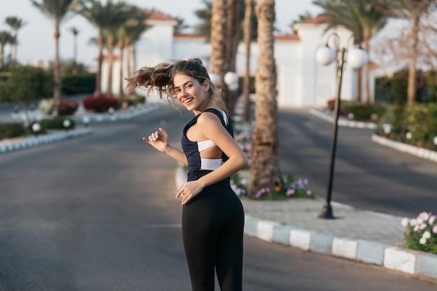 Sommerzeit der fröhlichen jungen Frau, die auf der Straße in der tropischen Stadt läuft. Lächeln in die Kamera, fröhliche Stimmung, Spaß, Training, sonniger Morgen, attraktives Model