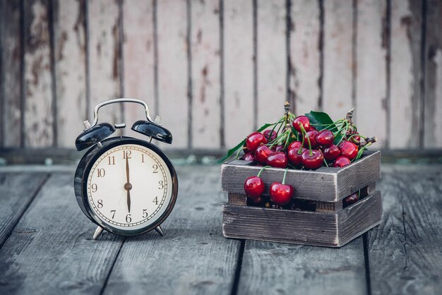 Sommerzeit, rote Kirsche und ein Wecker auf einem alten Holztisch