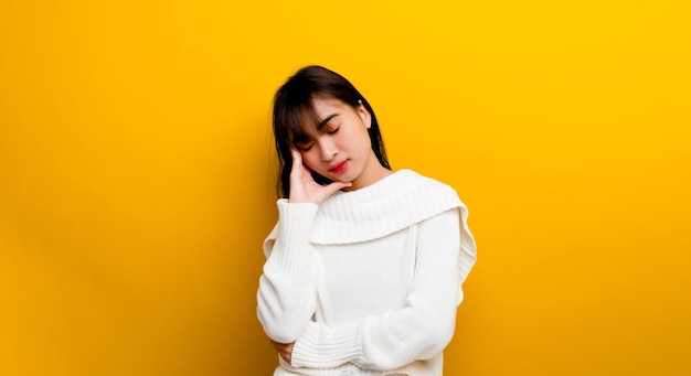 Somnolencia. Una hermosa mujer con un suéter blanco. Cansado, bostezando, cansado, con las manos cubriendo la boca, los ojos cerrados y soñoliento en un fondo amarillo