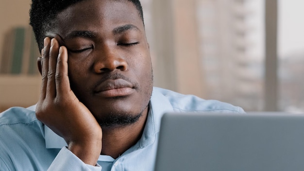 Somnoliento hombre africano cansado hombre de oficina hombre soñador hombre de negocios tiene problemas para dormir siesta descanso en el escritorio