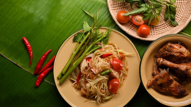 Somtum- oder Papaya-Salat und gegrilltes Hähnchen im thailändischen Stil auf Bananenblätter-Hintergrund-Draufsicht