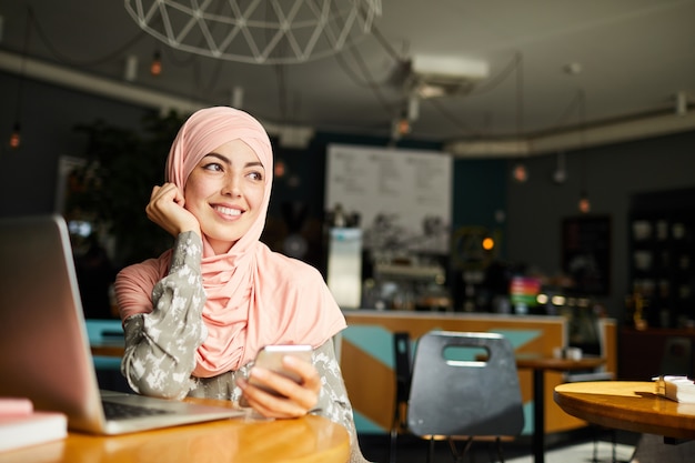 Soñadora mujer musulmana feliz con teléfono inteligente