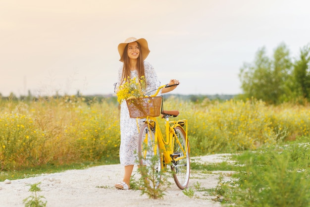 Soñando jovencita está sosteniendo su bicicleta mientras camina con ella en un campo de flores amarillas