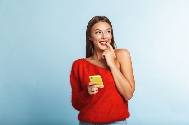 Soñando pensando mujer joven posando aislada, mediante teléfono móvil.