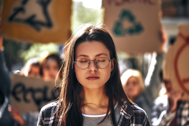 Soñando con tierra limpia mujer joven en gafas manteniendo los ojos cerrados mientras está de pie al aire libre en