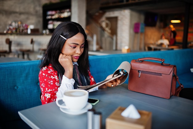 Sonfident joven mujer afroamericana en ropa casual elegante en el menú de lectura de café