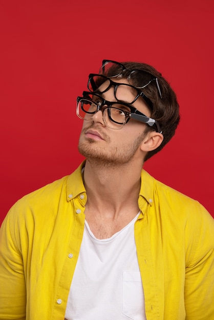 sonhador homem bonito engraçado na camisa amarela com muitos óculos no rosto olhando para longe isolado em fundo vermelho