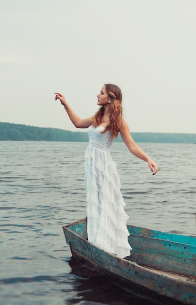 Sonhadora menina loira de vestido branco no antigo lago de barco