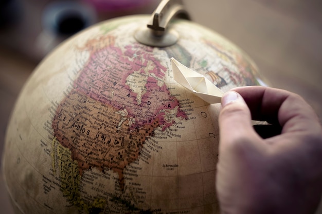 sonhadora wanderlust pessoas mão brincando com barquinho de papel em uma esfera do mundo globo escolhendo e imaginando para viajar e chegar a um novo destino. planejamento de férias e estilo de vida