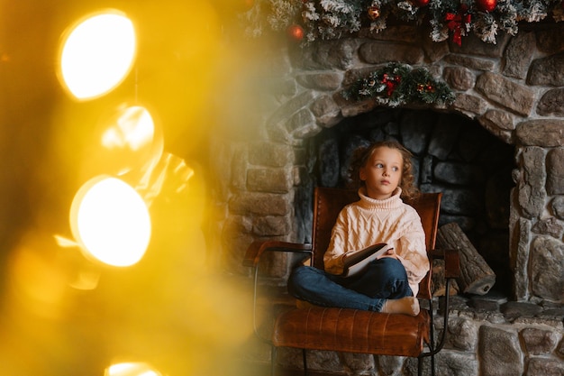 Sonhando pensativa garotinha loira cacheada escrevendo carta para o papai noel, sentada na cadeira