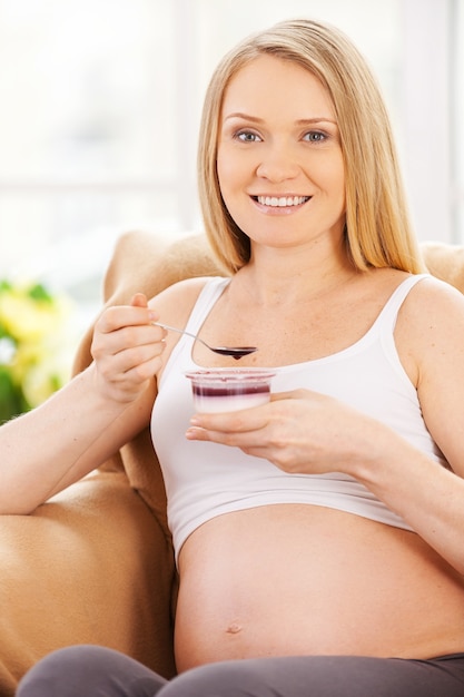 Sonhar acordado da mulher grávida. Mulher grávida feliz sentada na cadeira comendo iogurte