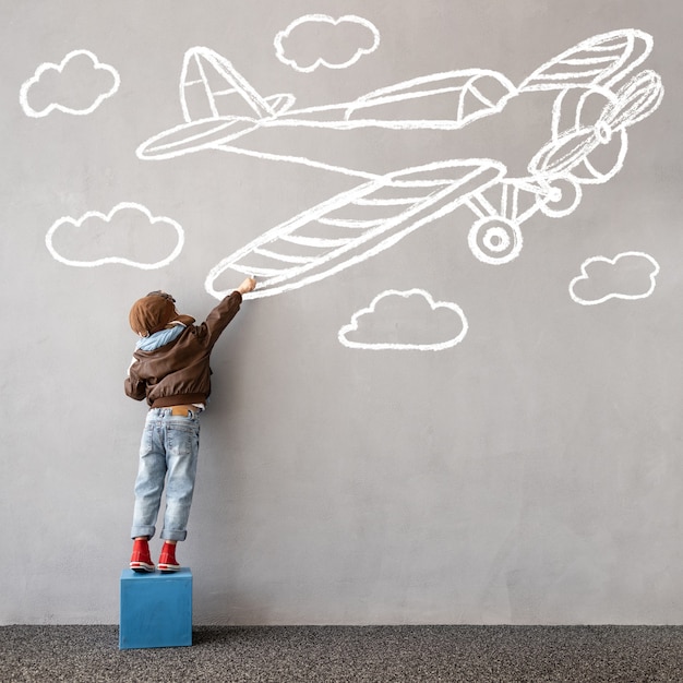 Sonhe grande! Criança feliz desenha um avião de giz na parede. Imaginação infantil e conceito de viagem