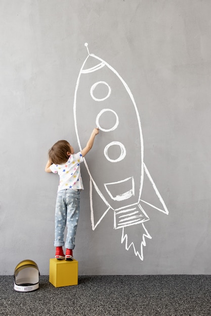 Sonhe grande! Criança feliz desenhando um foguete de giz na parede