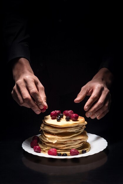 Sonho de morango. Perto das mãos do homem decorando os panquecas enquanto usa frutas e cozinhando no restaurante.