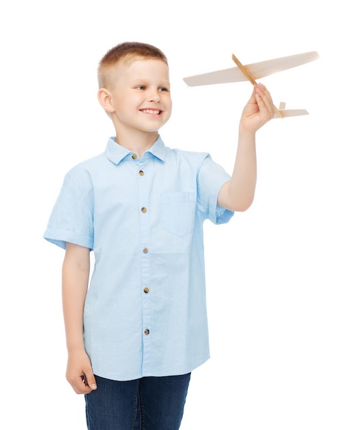 sonhos, futuro, hobby e conceito de infância - menino sorridente segurando um modelo de avião de madeira na mão