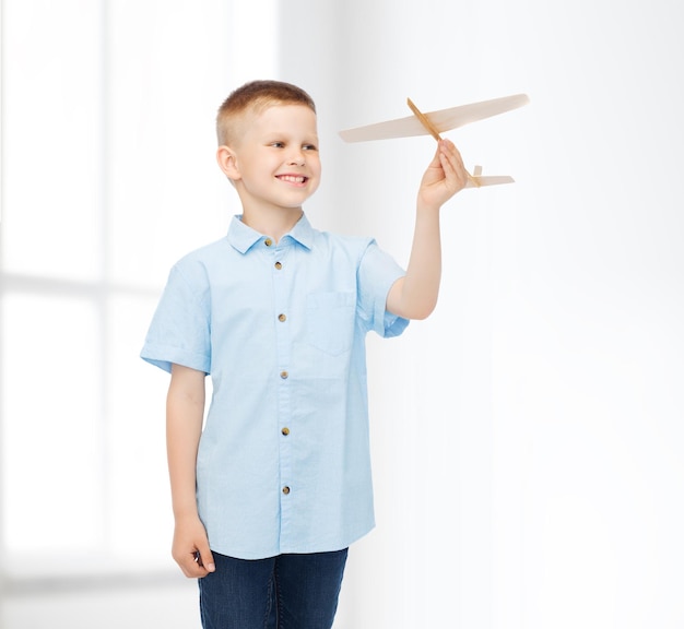 sonhos, futuro, hobby, lar e conceito de infância - menino sorridente segurando o modelo de avião de madeira na mão sobre o fundo do quarto branco