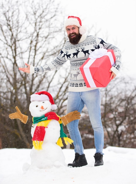 Foto sonhos se tornam realidade. hipster feliz pronto para o natal. feriado de inverno. agasalho quente no tempo frio. homem santa dá presentes ao ar livre. homem barbudo construir boneco de neve. atividade da temporada de inverno. feliz natal.