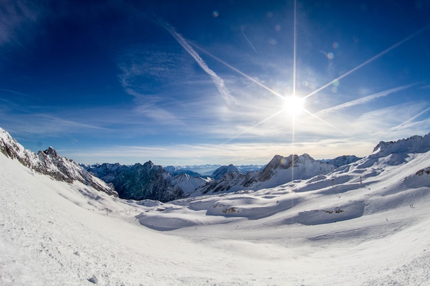 Sonne auf der Skipiste und Panorama der schneebedeckten Alpen vom Skigebiet