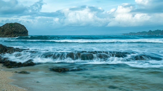 Foto sonnenaufgang am bengkung-strand in malang, indonesien wellen, steile felsen und blaue wolken