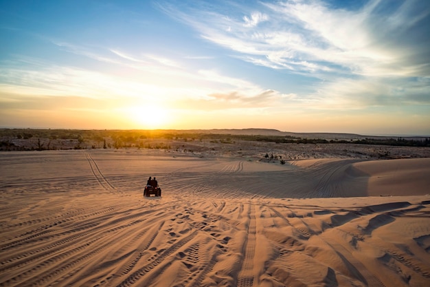 Sonnenaufgang in der Wüste. Szene mit zwei ATV-Bikern. Touristen fahren auf einem Gelände-Quad durch die Sanddünen der vietnamesischen Wüste. Safari am frühen Morgen in MUI ne Vietnam.