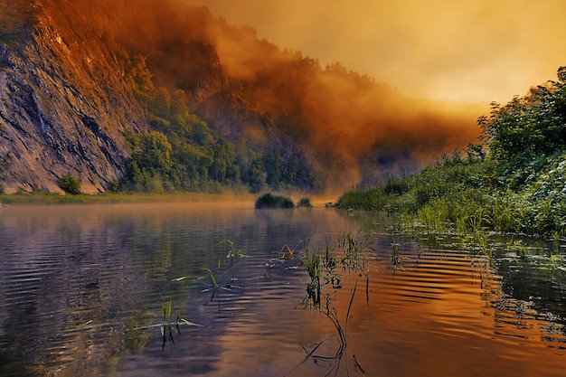 Sonnenaufgang malt den Morgennebel über dem Fluss in hellen und gesättigten orange-gelben Farben