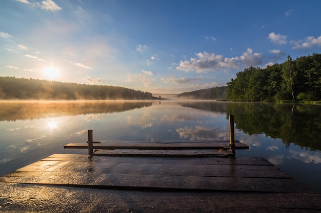 Sonnenaufgang über dem nebligen Fluss mit einem Holzsteg